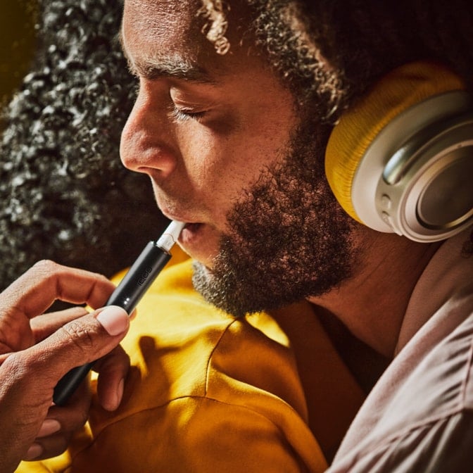 A bearded man using an Obsidian Black IQOS ILUMA PRIME device. 