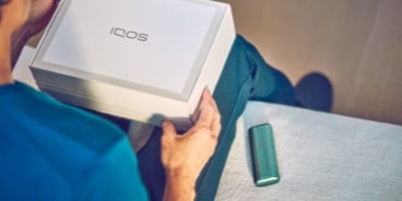 Hands unboxing an IQOS device.