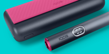 Red and black IQOS ILUMA i PRIME device and its charger on a light turquoise background