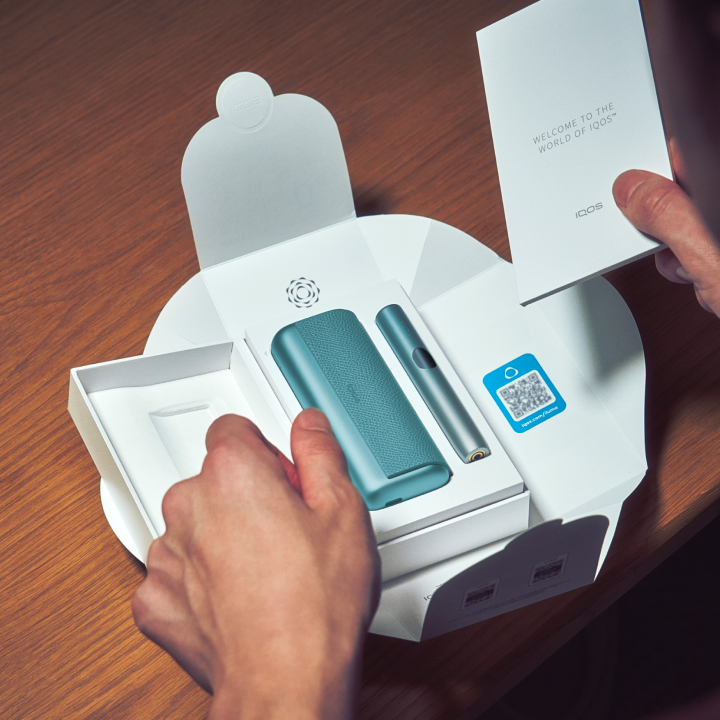 Detail of hands unboxing a blue IQOS ILUMA i PRIME device