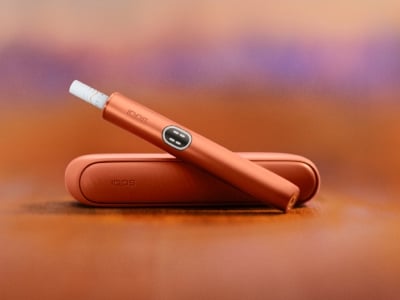 Terracotta IQOS ILUMA i Gerät über seinem Charger, mit rotem Hintergrund