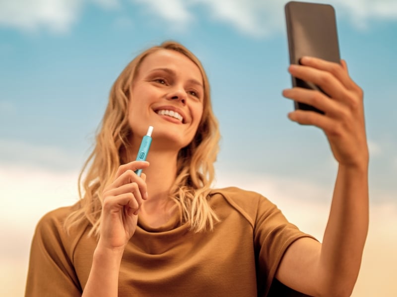 Woman looking at her phone while holding an IQOS ILUMA i device