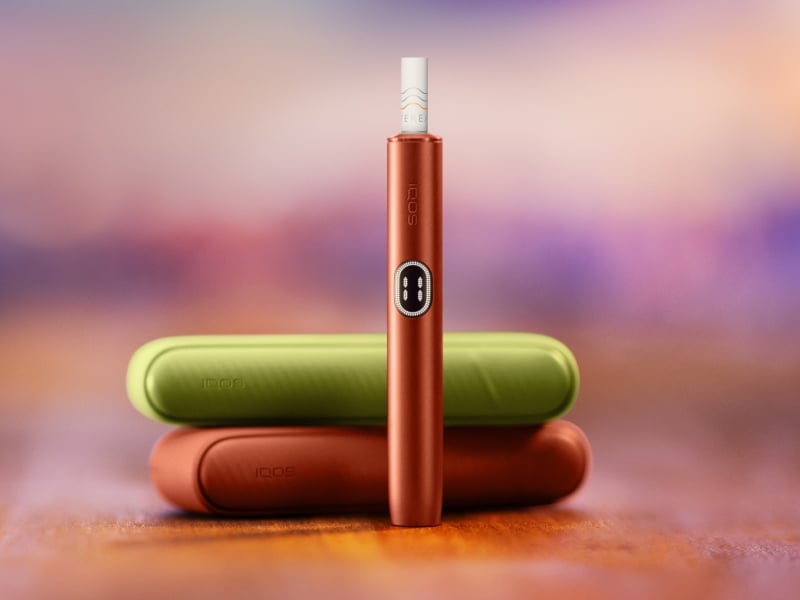 IQOS ILUMA i device standing in front of two chargers of different colours