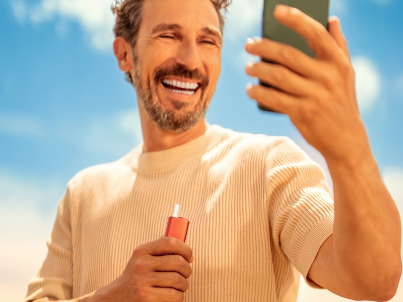 Man looking at his phone while holding an IQOS ILUMA i ONE device