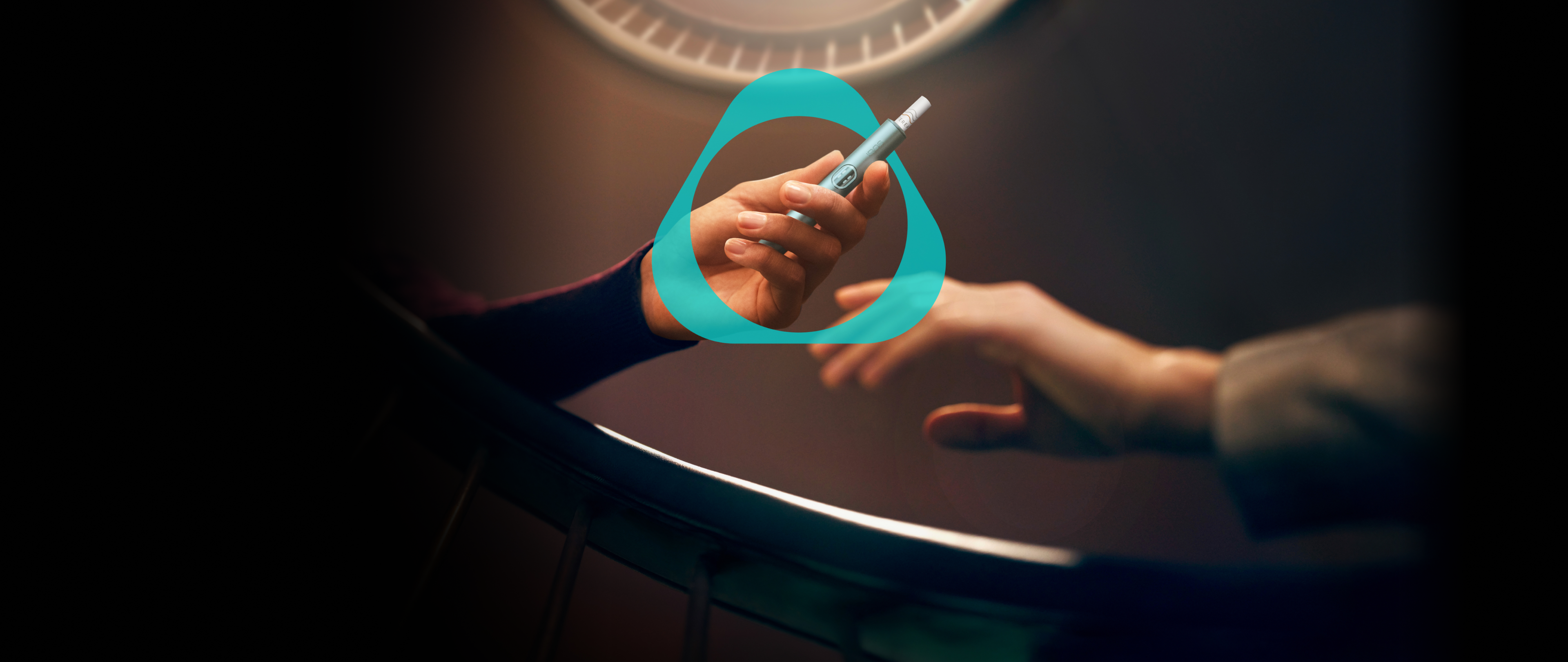 Dunkler Treppenhintergrund - Hände halten IQOS Gerät mit Tabakstick - mit IQOS Logo