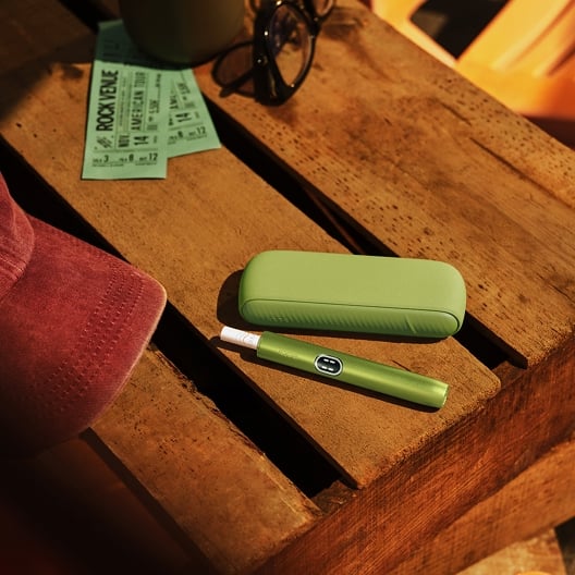 Outdoor scenary - Green IQOS ILUMA i device with tobacco stick on a table