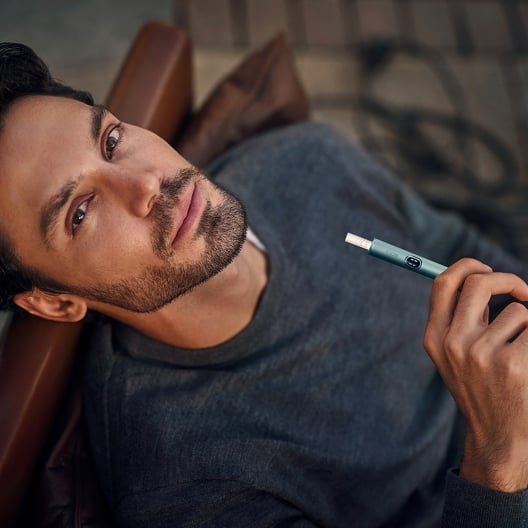 Balcony scenary - Man holding IQOS ILUMA device with tobacco stick