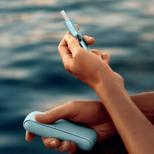 Outdoor scenary with lake view - Hand holding IQOS ILUMA i device, with charger 