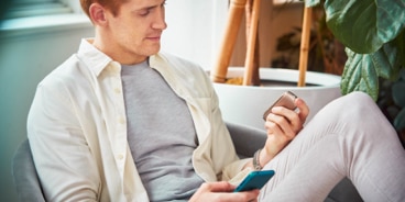 Man on a couch with his IQOS kit and the mobile in his hands