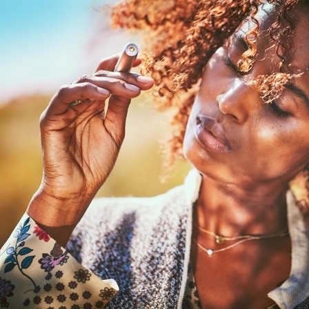 A woman with curly hair holding an IQOS device. 