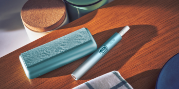Blue IQOS ILUMA i PRIME device and its charger on a wooden table
