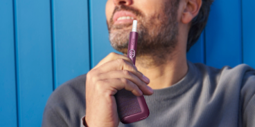 Man holding a garnet red IQOS ILUMA i PRIME device and its charger