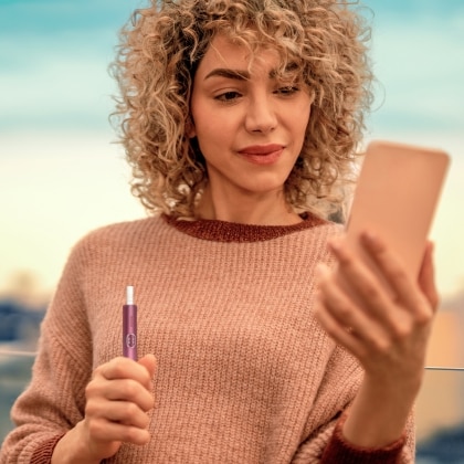 Woman looking at her phone while holding an IQOS ILUMA i PRIME device