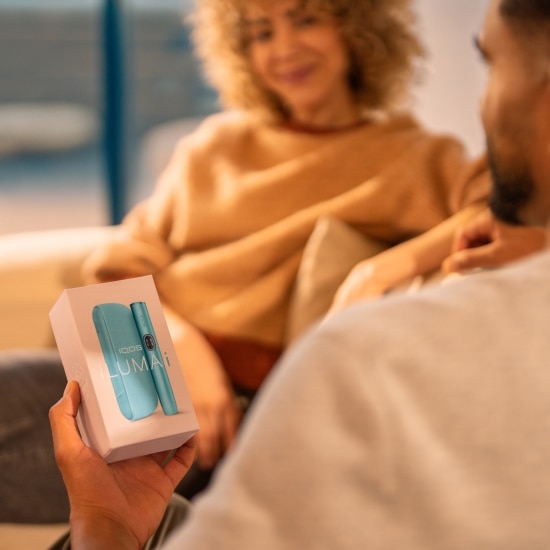 Uomo con in mano una confezione contenente un dispositivo IQOS ILUMA i, seduto di fronte a una donna