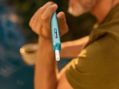 Hand holding a blue IQOS ILUMA i ONE device