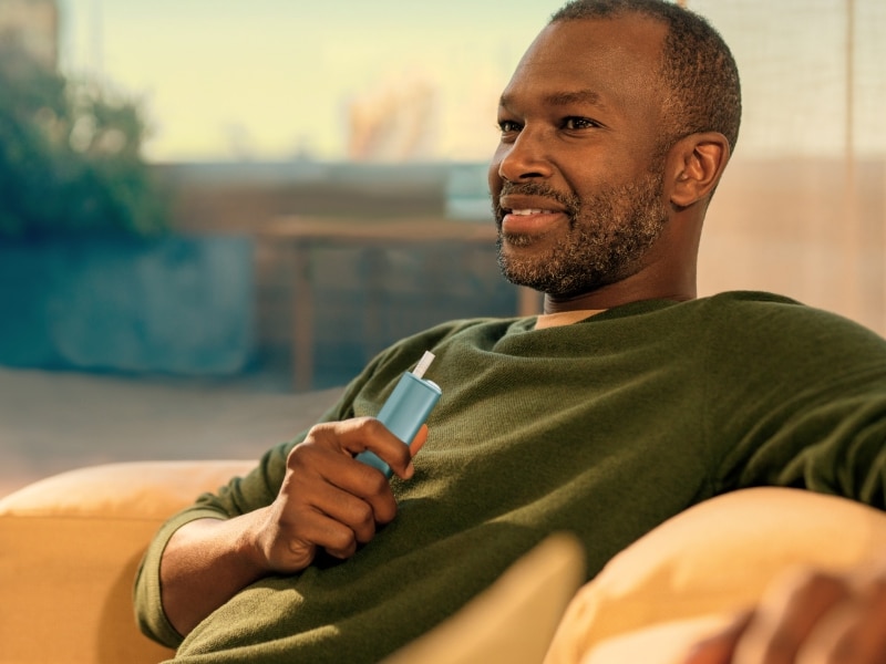 Uomo con in mano un dispositivo IQOS ILUMA i ONE, visto da sinistra