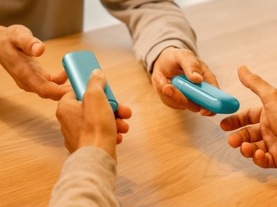 Hände, die zwei IQOS ILUMA Geräte austauschen