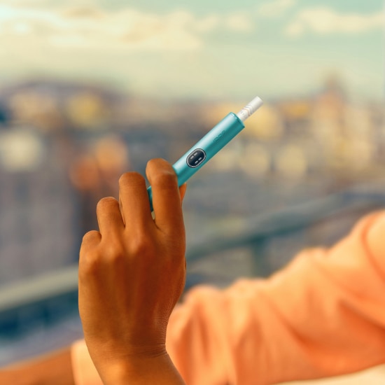 Hand, die ein IQOS ILUMA i Gerät hält, vor einem Balkon