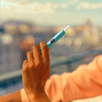 Hand, die ein IQOS ILUMA i Gerät hält, vor einem Balkon