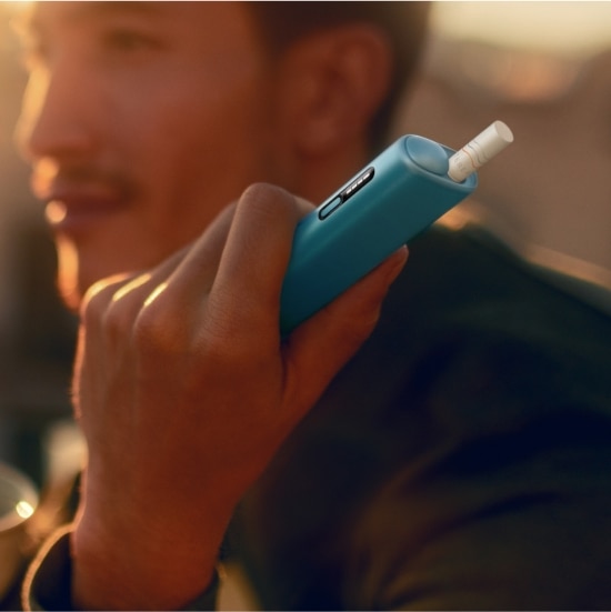 Uomo con in mano un dispositivo IQOS ILUMA i ONE, con tramonto sullo sfondo