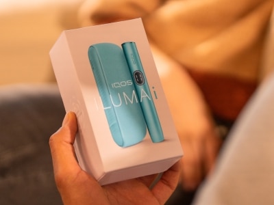 Mann mit einer IQOS ILUMA i Geräteverpackung, vor einer Frau sitzend