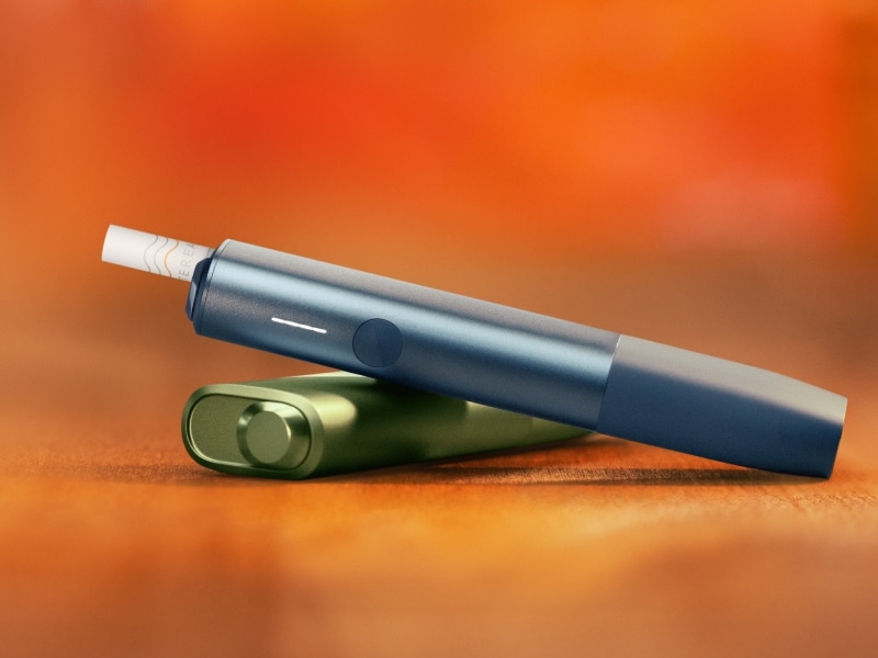 Blue IQOS ILUMA i ONE above a green IQOS ILUMA i ONE, with orange background