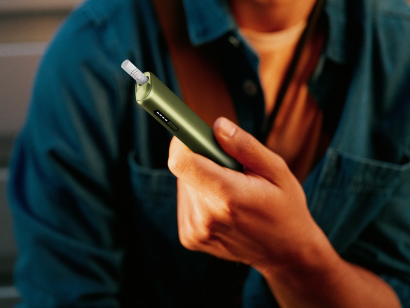 Hand holding a green IQOS ILUMA i ONE device
